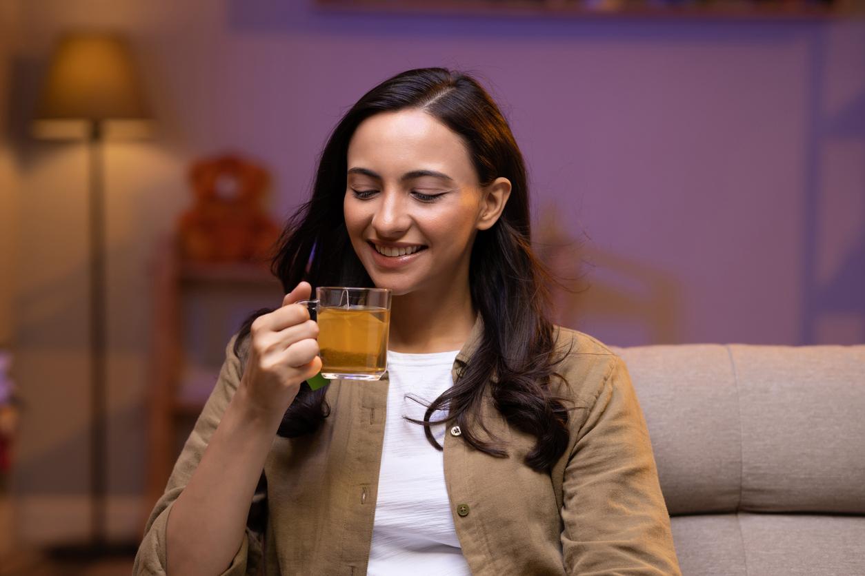 A smiling woman sips lemon gunpowder tea on her couch.