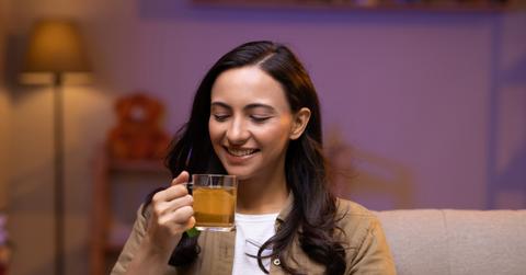 A smiling woman sips lemon gunpowder tea on her couch.