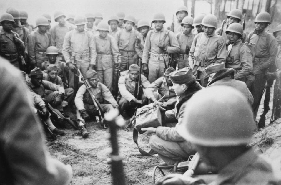 A black and white photo of soldiers at Camp Lejeune arranged in a circle while holding guns and wearing hard shell hats. 