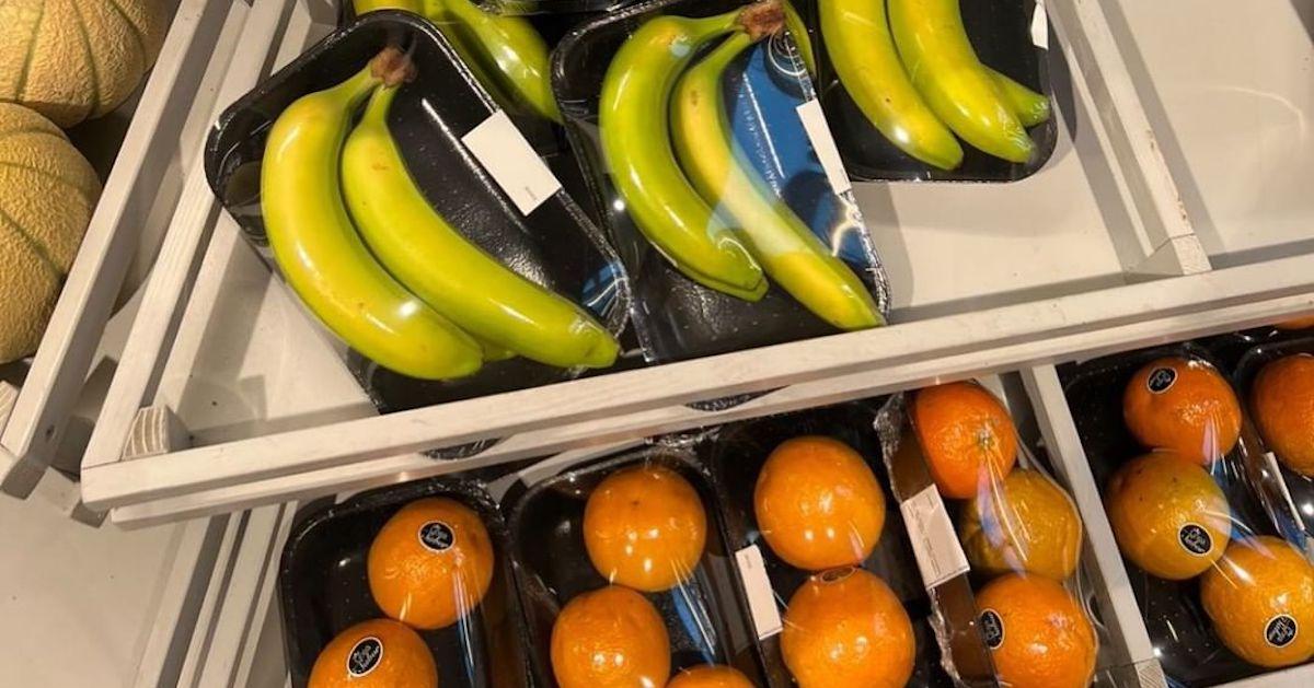 Bananas and oranges wrapped on plastic trays with cling film