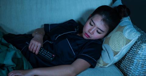 Photo of woman asleep on couch in front of TV while holding remote control