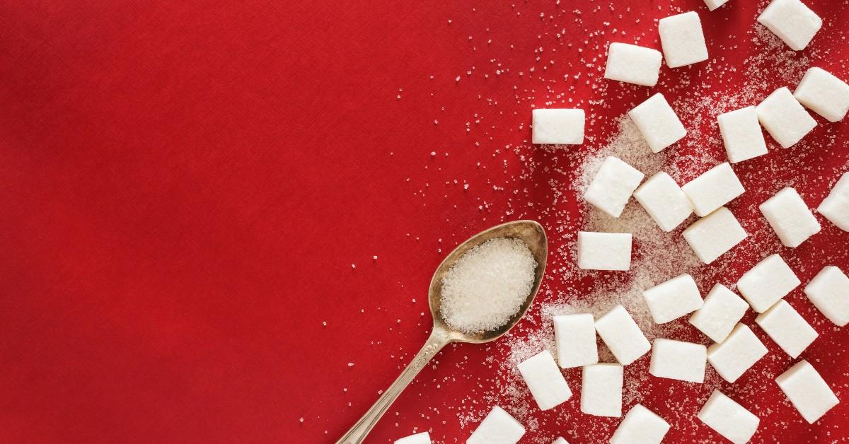 White sugar cubes sit next to a gold spoon on a red background 