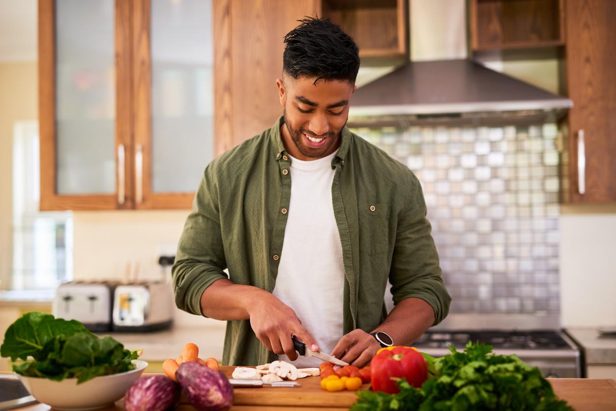 A smiling vegan man chops vegetables in the kitchen for dinner.