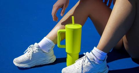 Photo of a lime green Simple Modern beverage tumblr sitting in between legs in front of a blue background