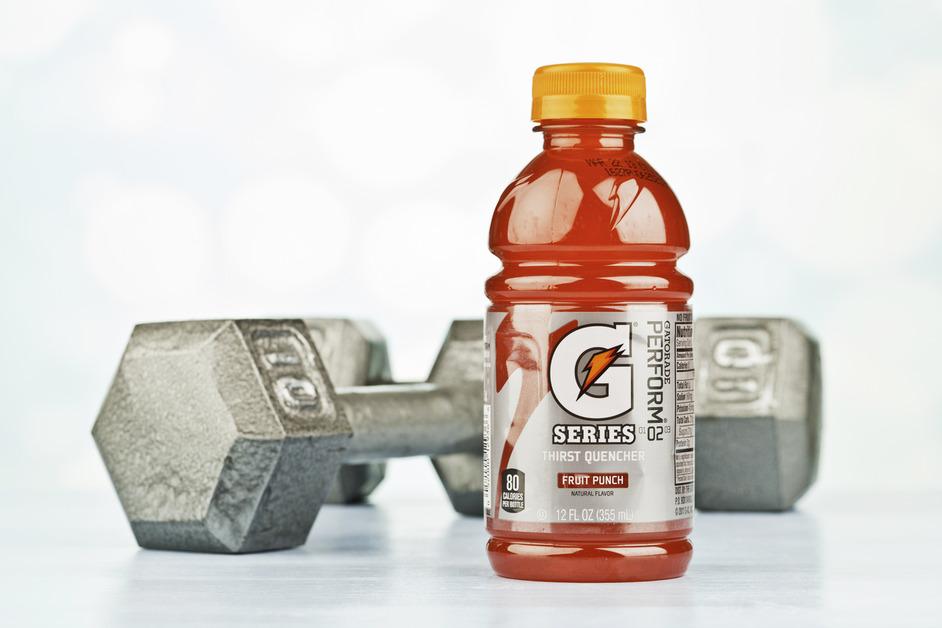 A bottle of red Fruit Punch flavored Gatorade sits in front of a pair of ten pound weights. 