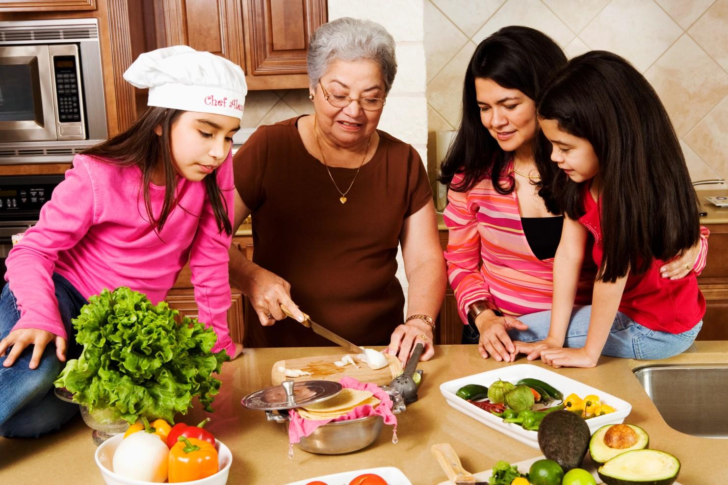 A grandmother prepares food with her daughter and granddaughters in a kitchen.