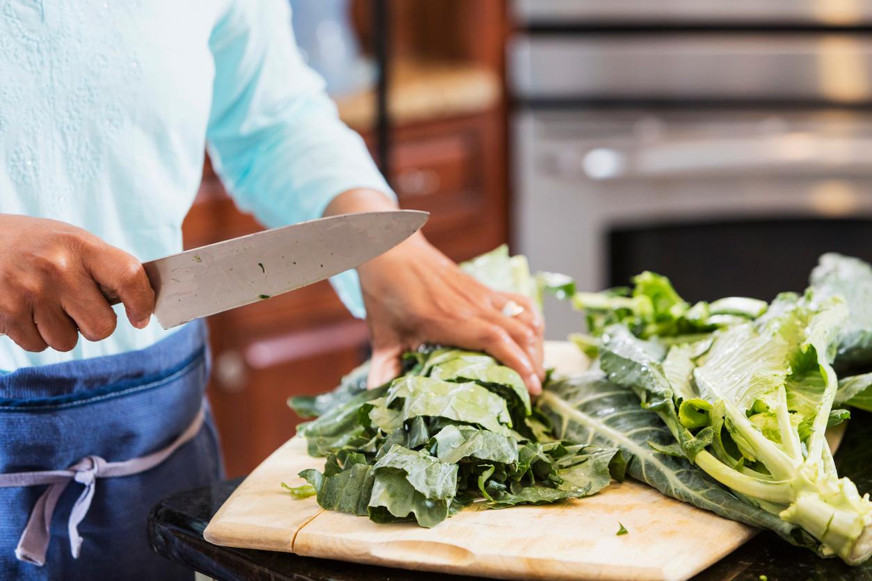 A person wearing a blue shirt prepares a bunch of collard greens with a large chef's knife.