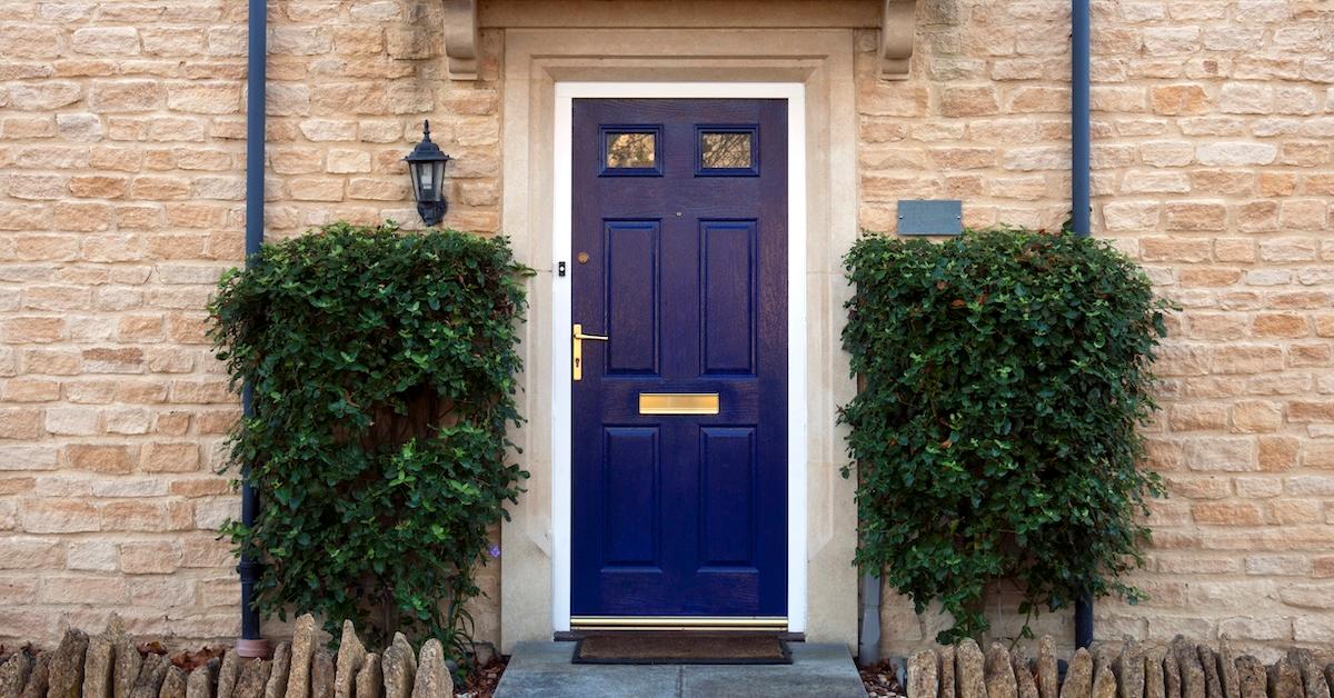 Blue door on tan brick house with two shrubs