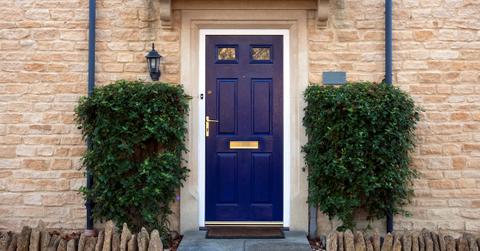 Blue door on tan brick house with two shrubs
