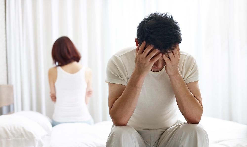 A man and a woman sitting on opposite sides of a bed upset.