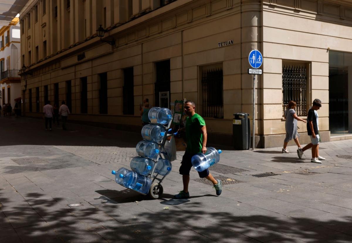 man pushing large water jugs through city streets