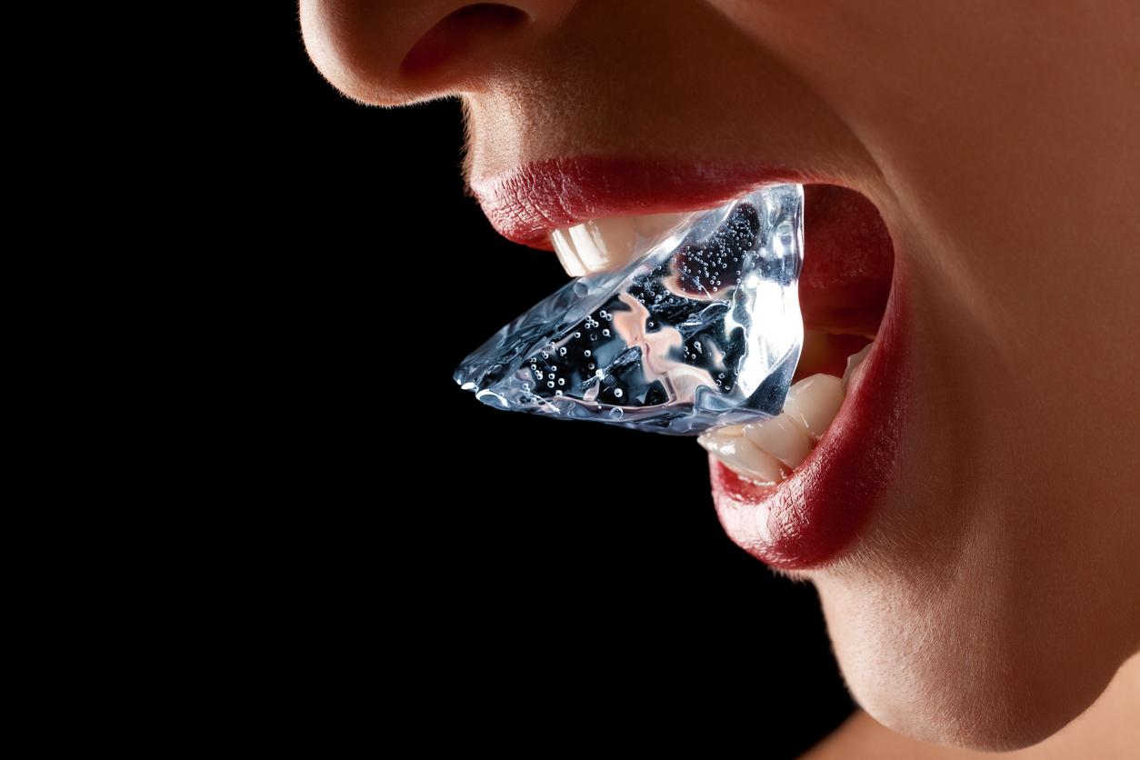 A woman with lipstick holds an ice cube in her mouth.