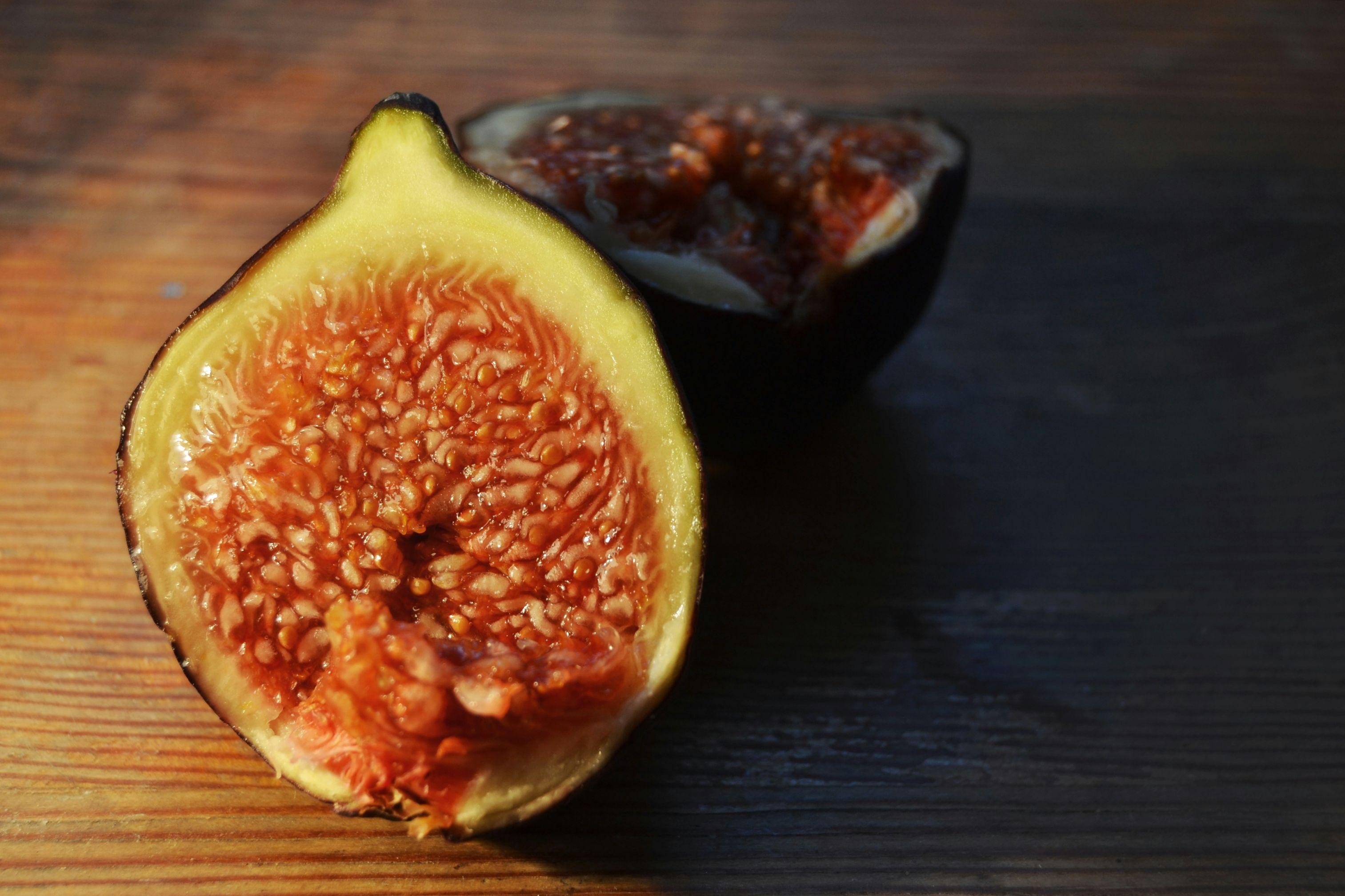 A close-up photo of the inside of a halved fig, with both halves sitting atop a wooden table.