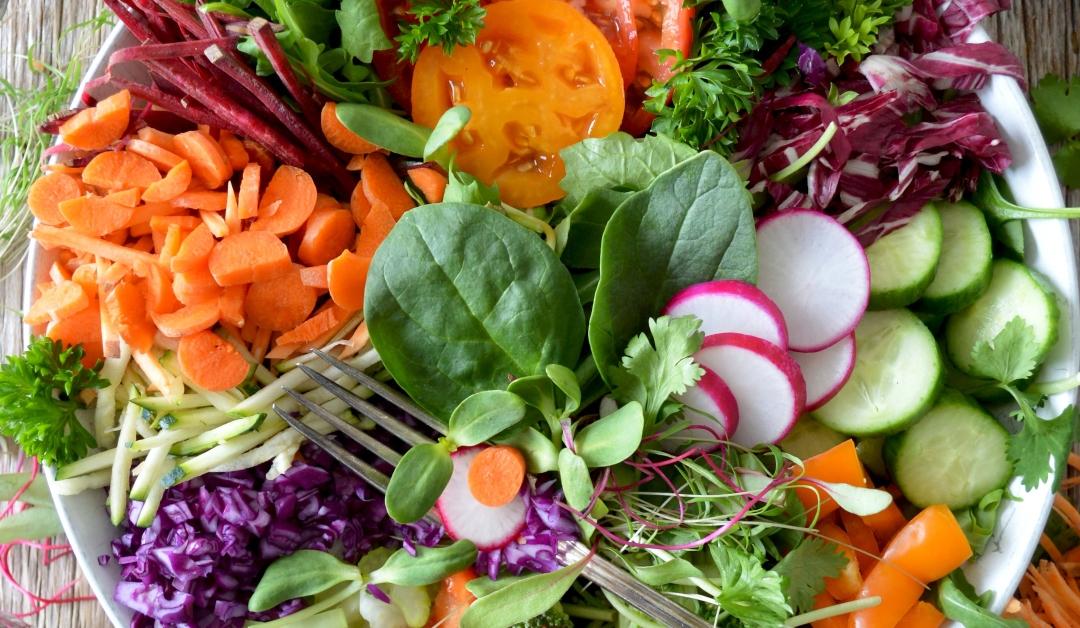 A plate full of fresh, colorful vegetables, including spinach, carrots, beets, cucumbers, radishes, cabbage and tomatoes