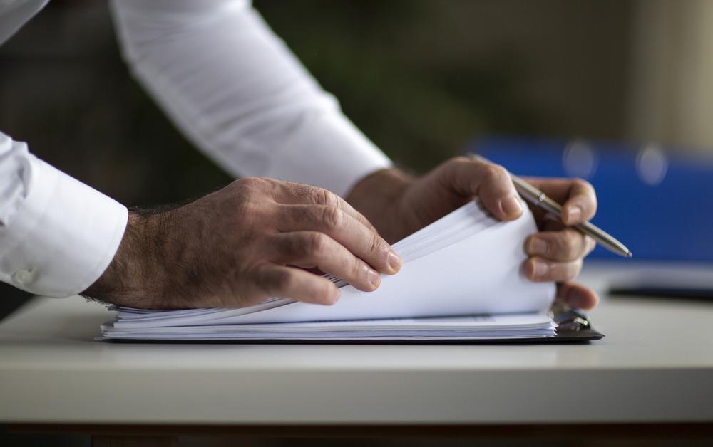 A close up of the hands of a person wearing a white shirt flips through a stack of white paper. 