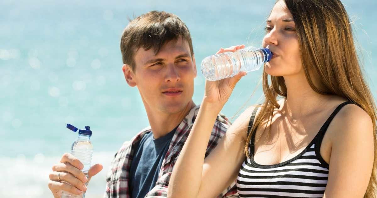 A man looks at a woman drinking bottled water at the beach (Representative Cover Image Source: Freepik | bearfotos)