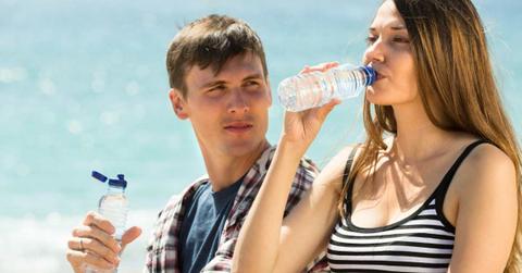 A man looks at a woman drinking bottled water at the beach (Representative Cover Image Source: Freepik | bearfotos)