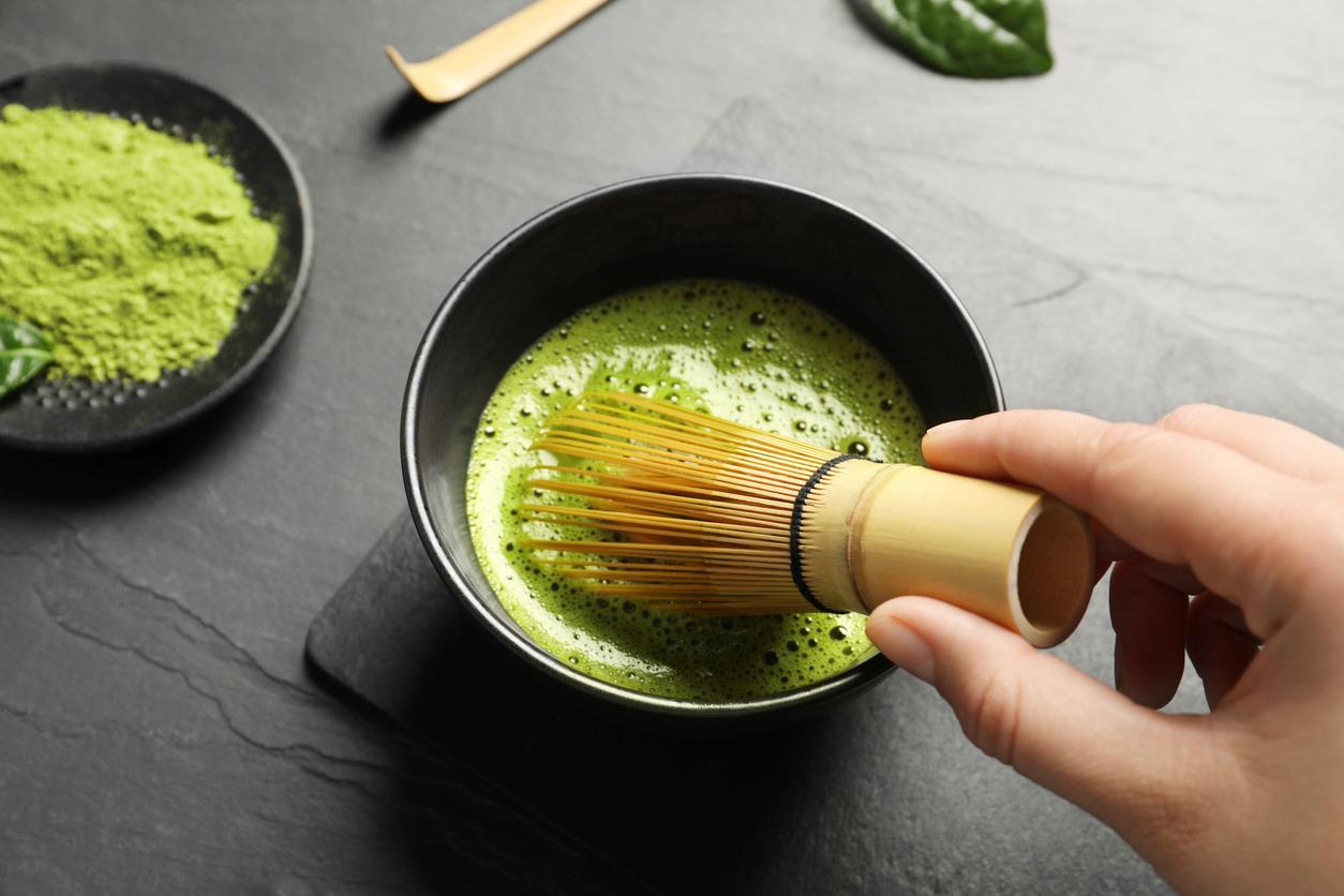 Close up of matcha powder and hot water being mixed together by a bamboo whisk.