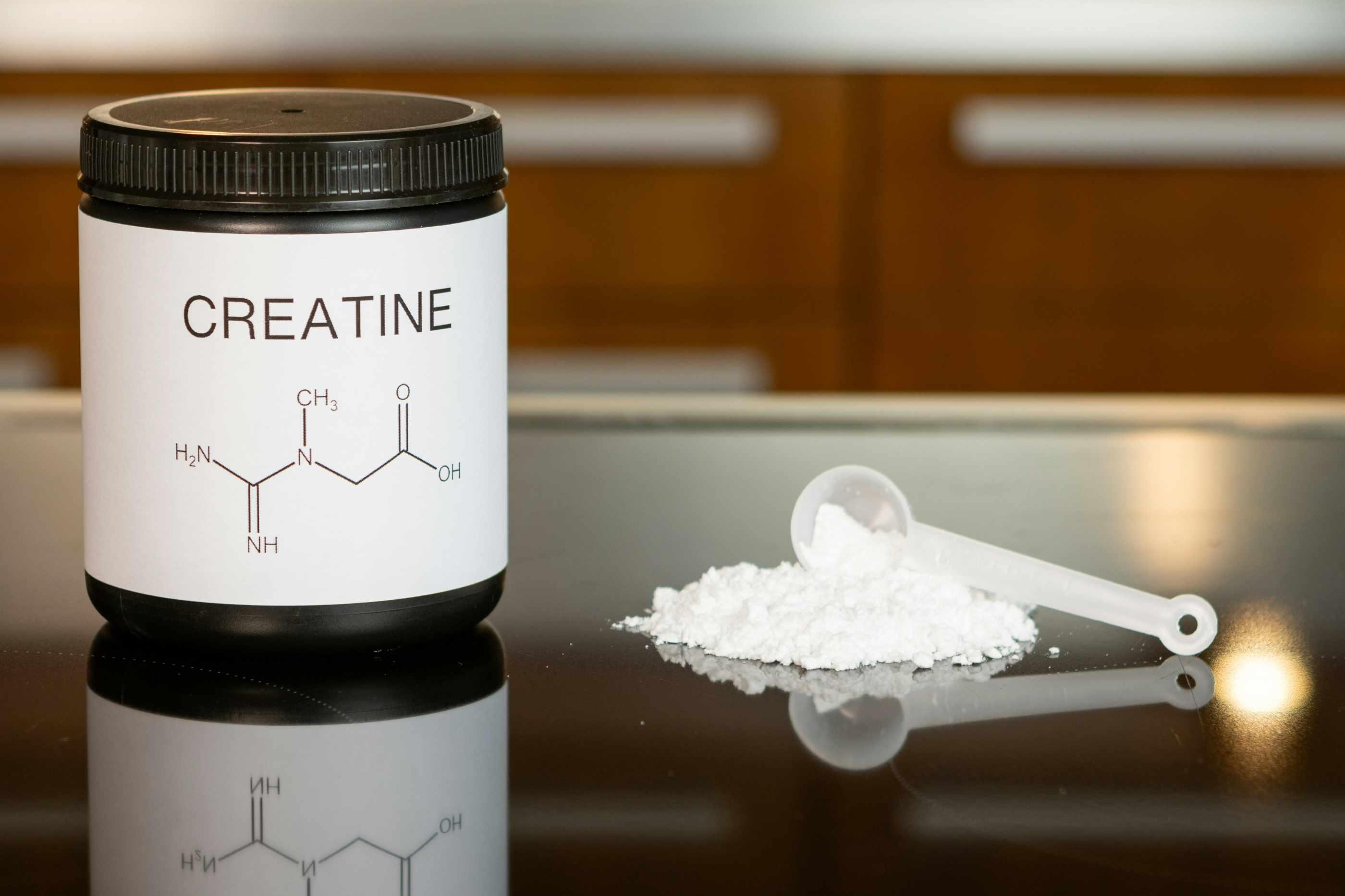 A bottle of creatine is pictured beside a scoop of powder.