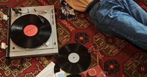Photo of two black vinyl records and a record player on the floor next to a person laying down partially out of frame