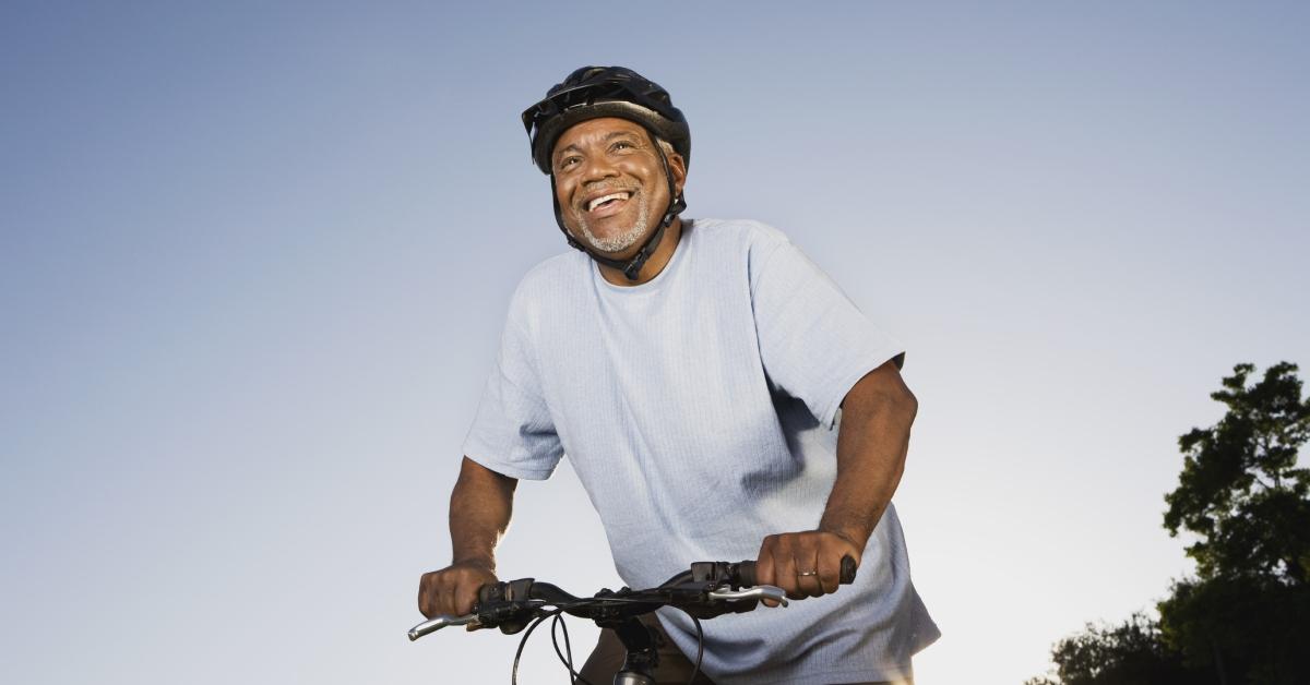 A  senior man smiles while he rides his bike in the evening.