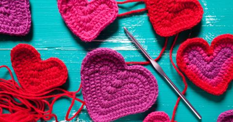 Close up of various sized purple and red crochet hearts scattered on a blue table.