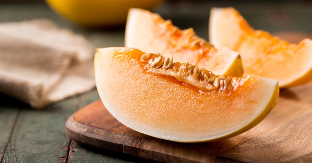 Cantaloupe sliced on a wooden cutting board.