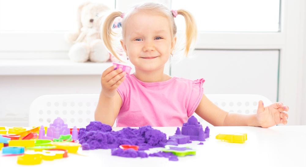 A young girl in a pink shirt playing with kinetic sand.