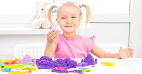 A young girl in a pink shirt playing with kinetic sand.