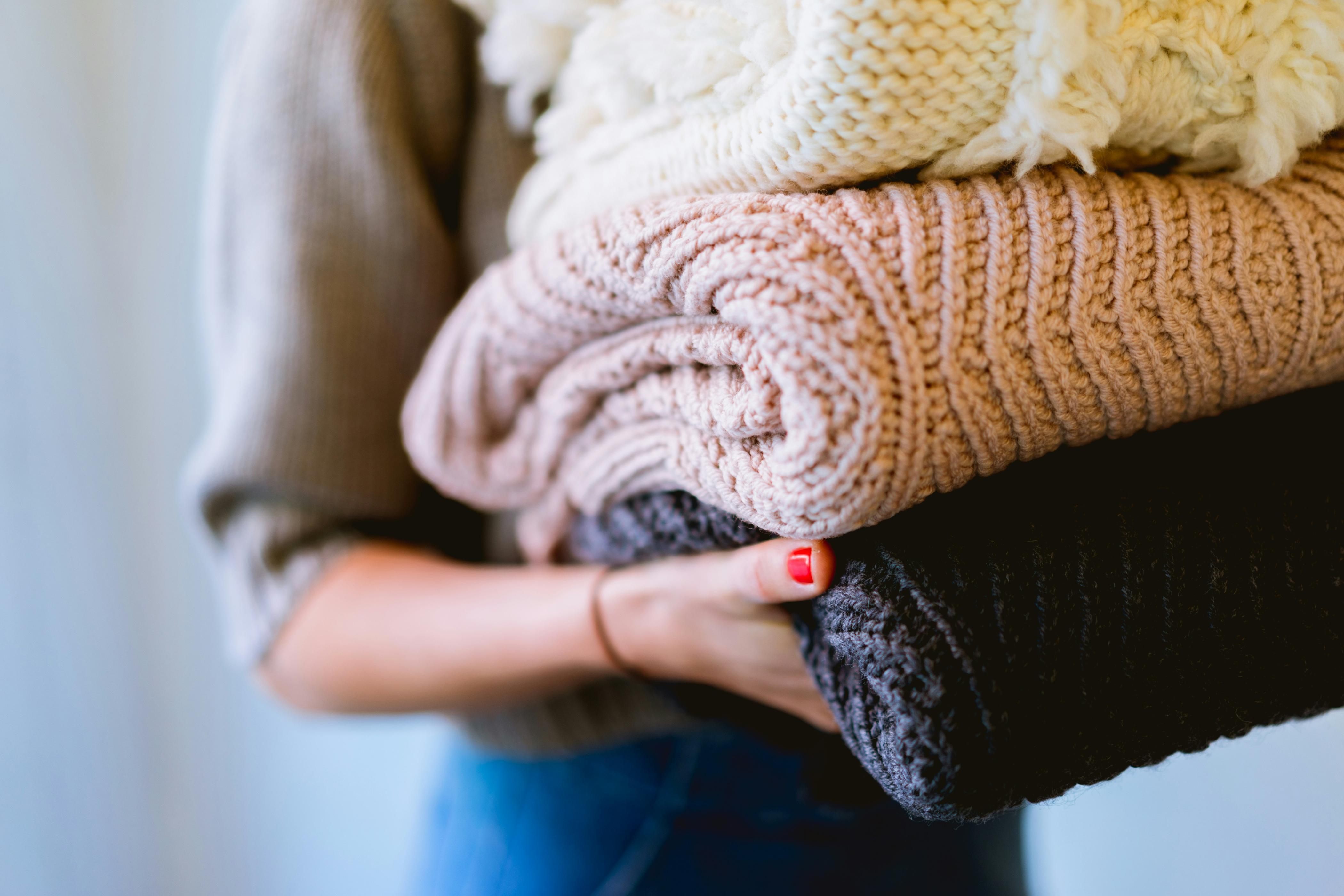 A woman holds a pile of knitted electric blankets in her hands as she walks to the laundry room.