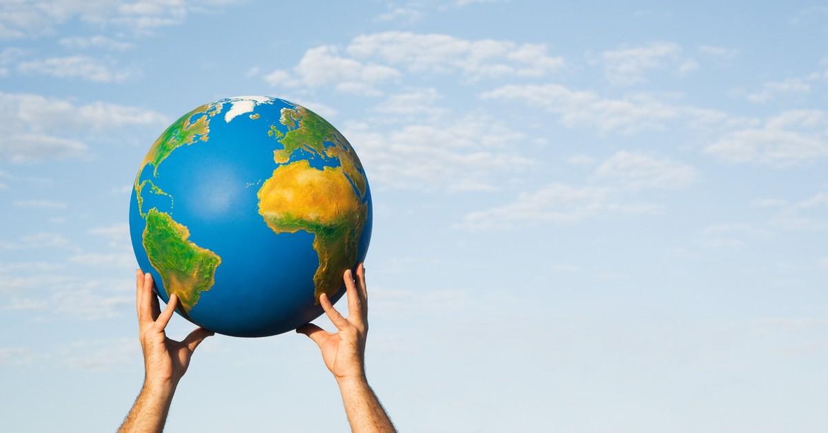 A pair of hands hold up a globe against the blue sky