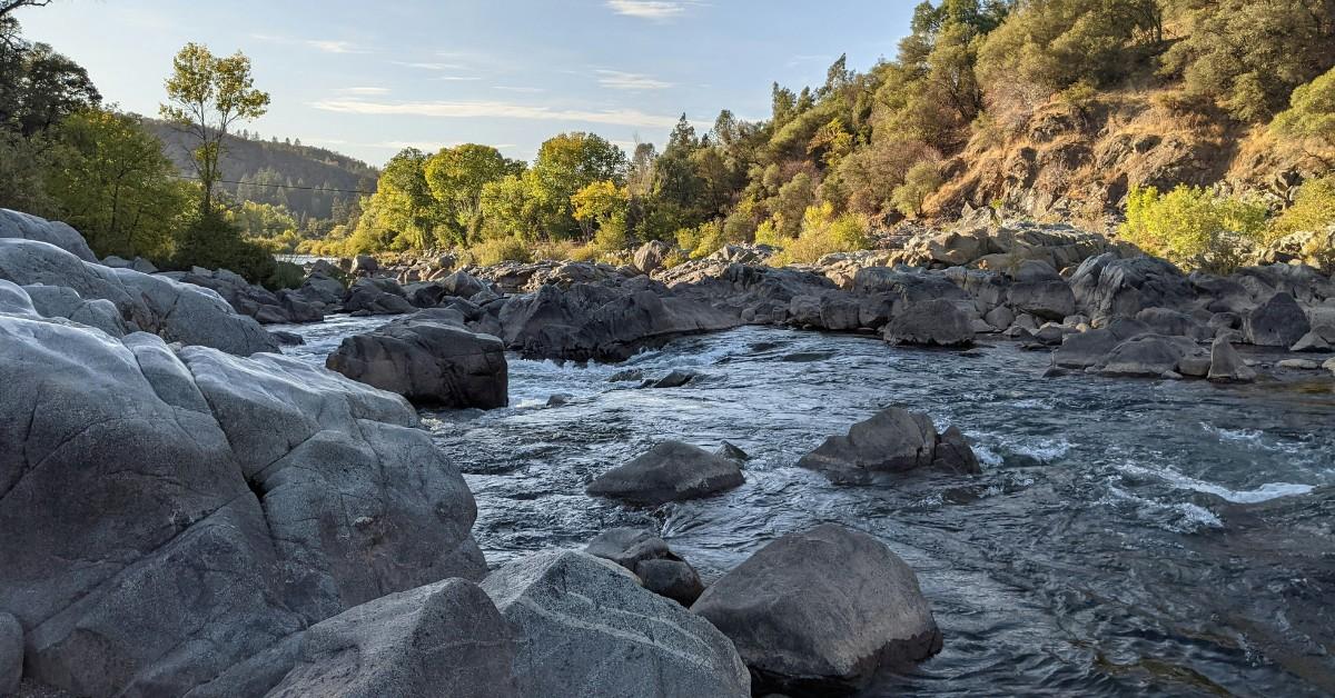 A river runs through a rocky area with trees and mountains surrounding it