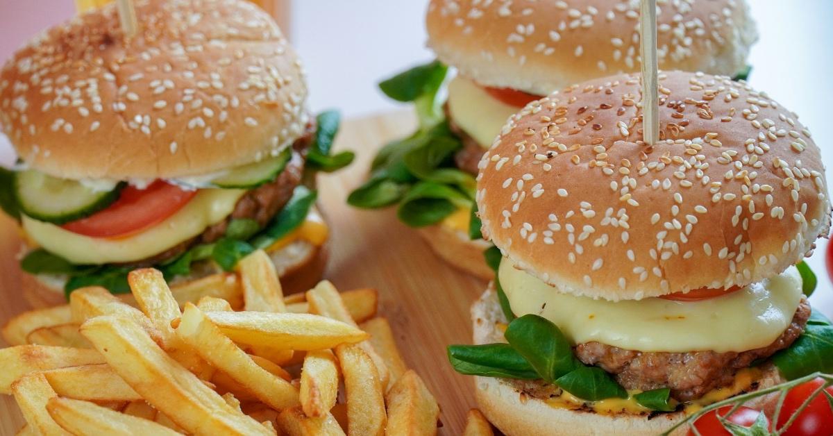 Two hamburgers with cheese, tomatoes, and pickles on a table with french fries.