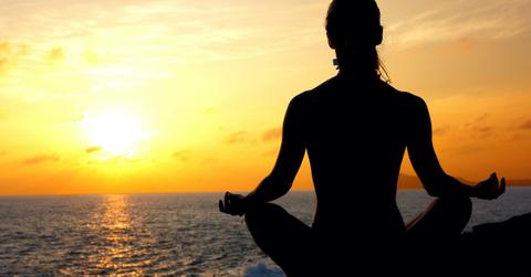 Silhouette of woman sitting crossed legged and meditating in front of sunrise over ocean