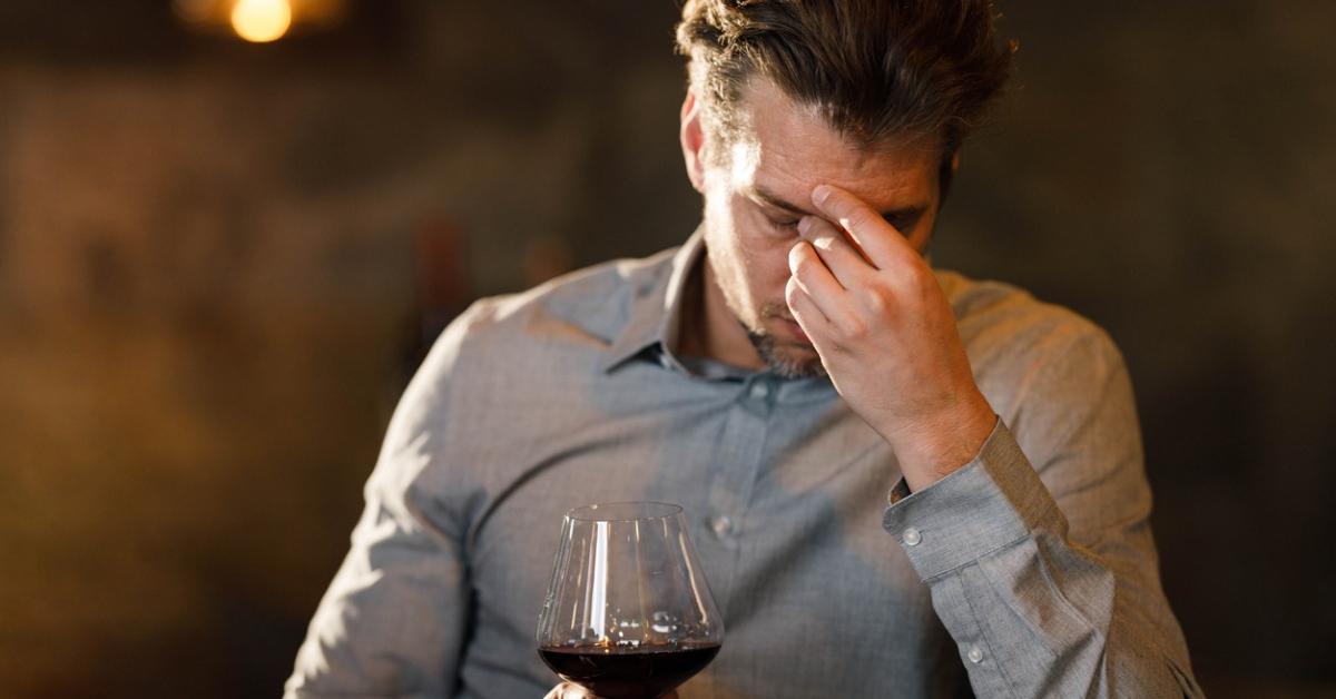 A guy with a headache drinking red wine.