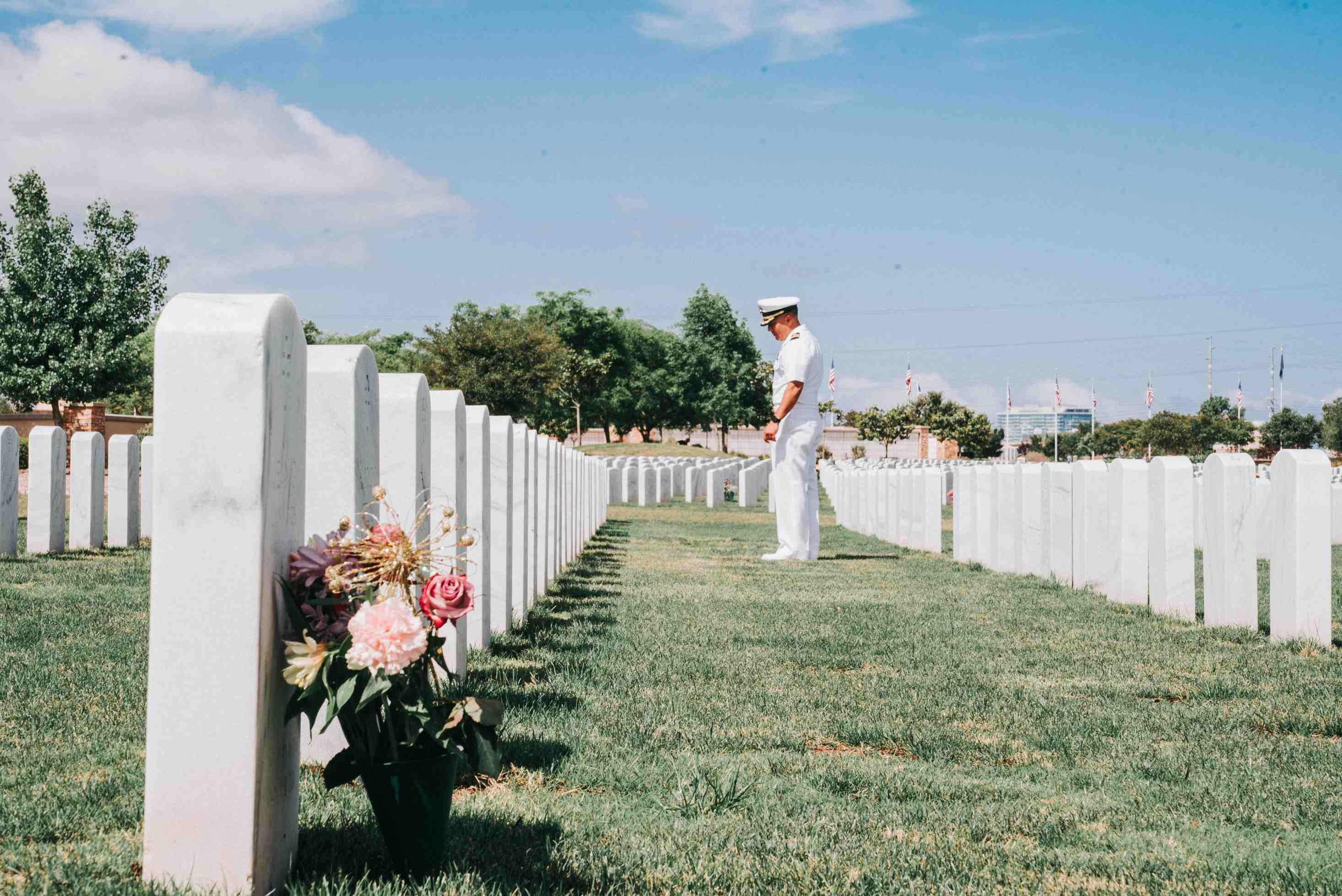 A military member in uniform mourns a colleague in front of their headstone in a cemetery.