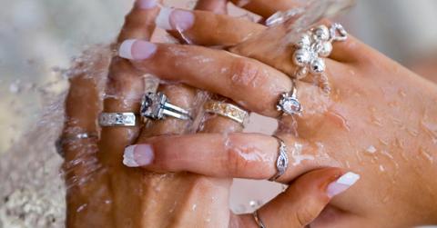 Close-up photo of manicured hands wearing several silver-toned rings under running water