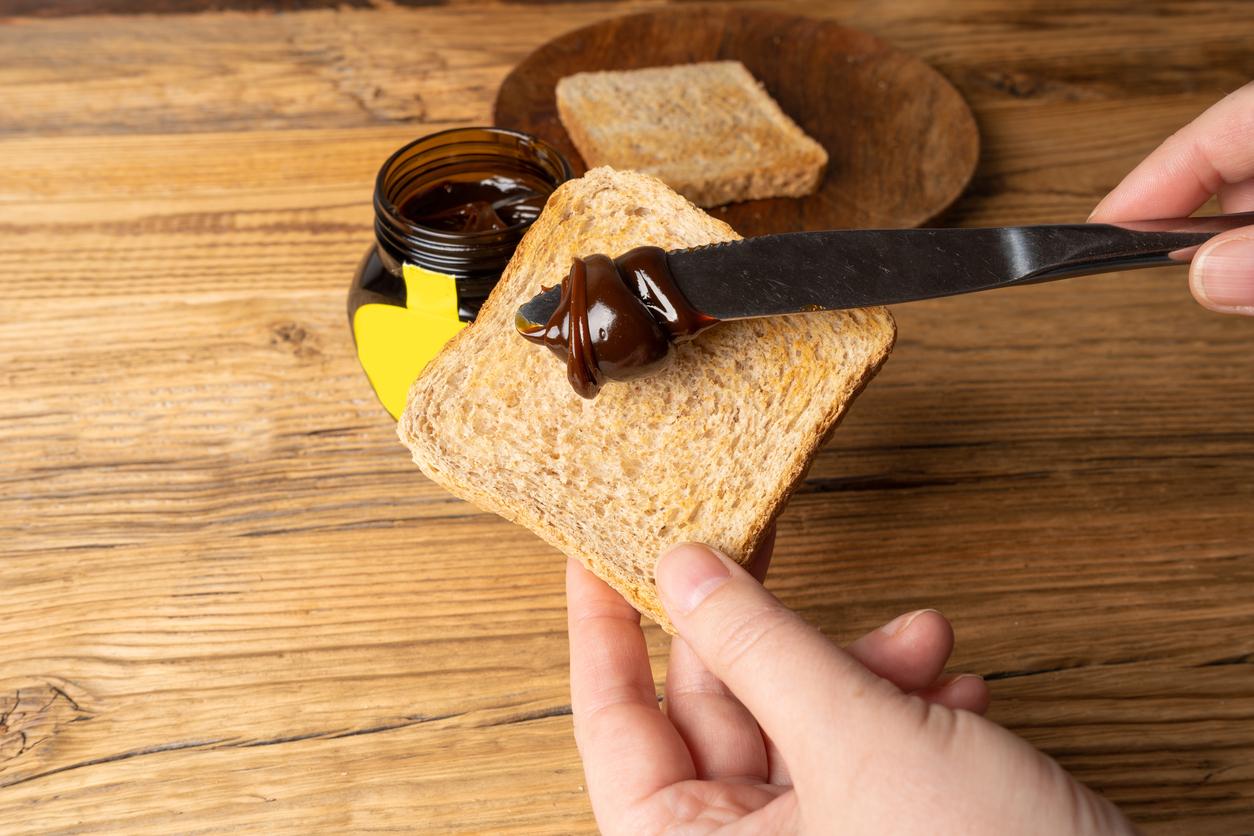 A person butters a piece of toast with Vegemite spread.