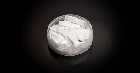 A plastic tin of nicotine pouches sits on a black background.