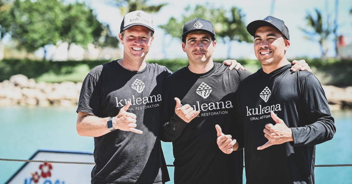 Three men on the beach wearing hats and smiling. 