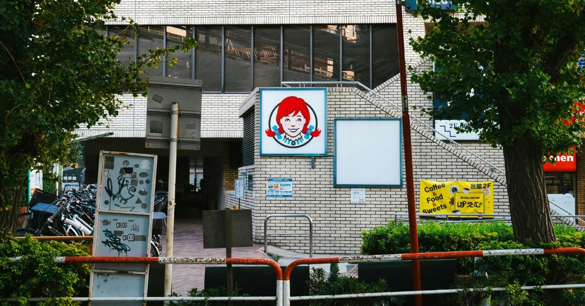 A small Wendy's sign is surrounded by other signs and graffiti against a brick wall