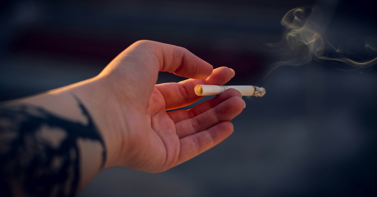 An outstretched hand holds a lit cigarette 