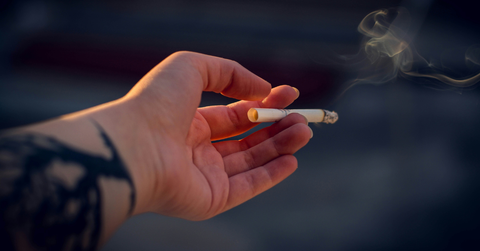An outstretched hand holds a lit cigarette