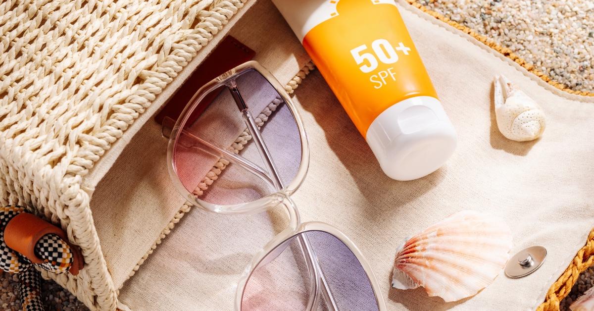 Sunscreen, sunglasses and seashells spilling out of a beach bag.