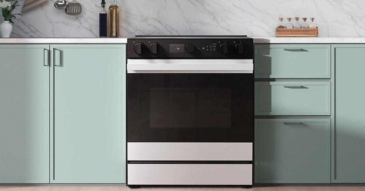 electric range in a kitchen with mint green cabinets and a marble backsplash