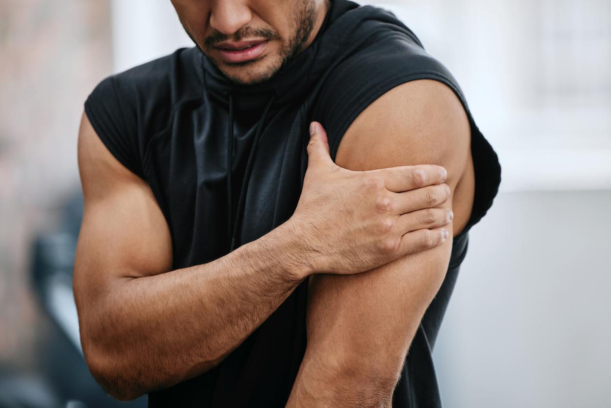 An athlete winces as he places his right hand over his sore muscles on his left arm.