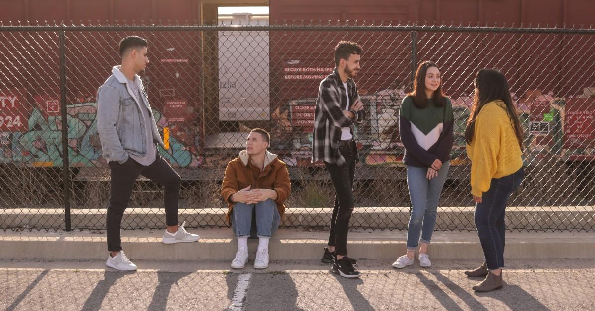 A group of teens stand in front of a chain link fence