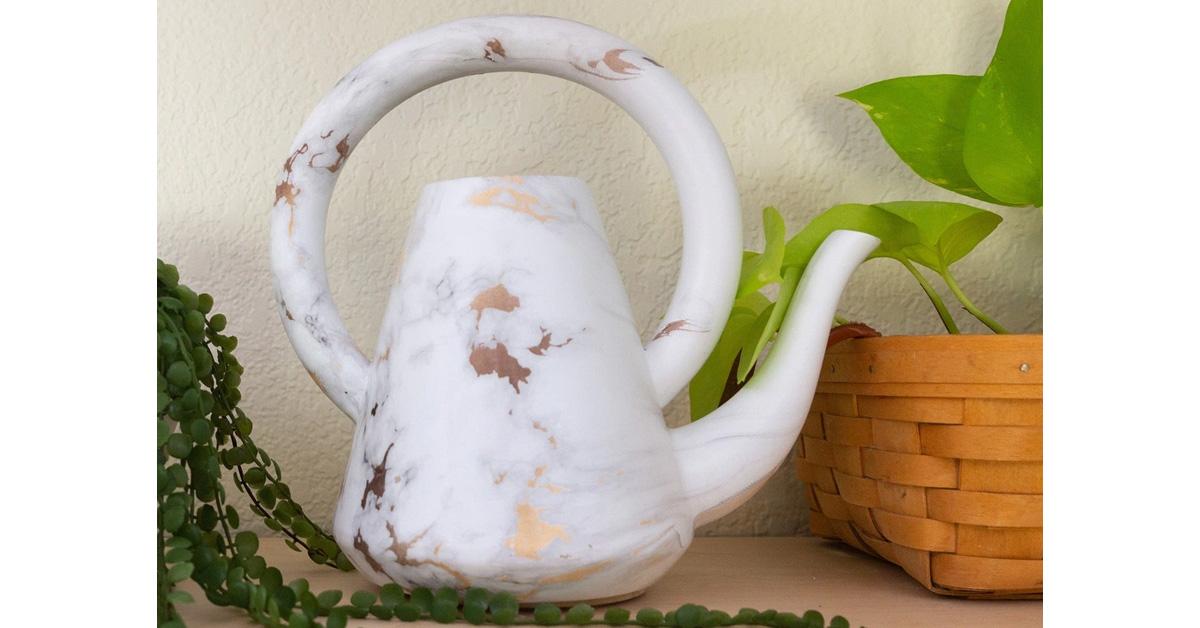 white and gold marbled ceramic watering can next to a basket and plants