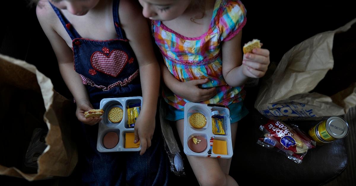 Two young girls, with their faces out of frame, eat Lunchables on their laps.