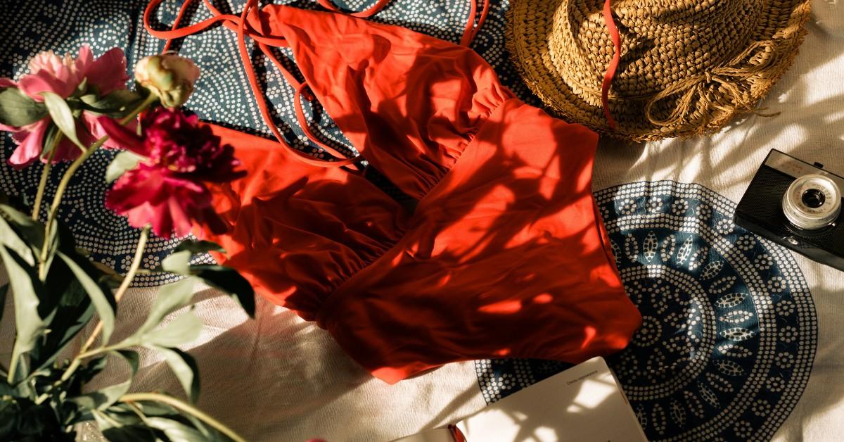 A red swimsuit lays on a bedspread with other travel essentials
